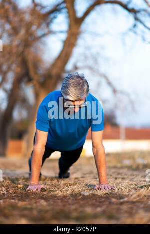 Hombre haciendo pushups senior en un entrenamiento al aire libre