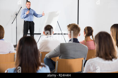 Profesor de pie masculinos positivos con micrófono en auditorio, ofreciendo  voz para grupo estudiantil Fotografía de stock - Alamy
