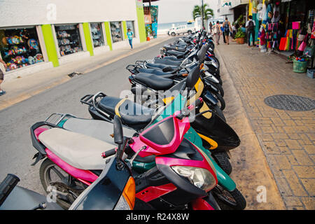 Colorido scooters o motocicletas para la venta o alquiler de pie en fila  con ruedas y luces en la calle al aire libre en Cozumel, México,  contratación transportat Fotografía de stock -