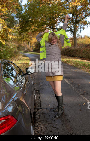 Mujer automovilista por su coche luchas para poner en una chaqueta de seguridad reflectantes Foto de stock