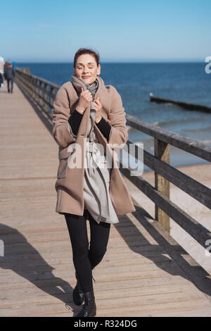 Mujer vistiendo leotardos y un abrigo caminando a lo largo de un muelle de sobre mar en calma en soleado día de invierno Fotografía de stock - Alamy