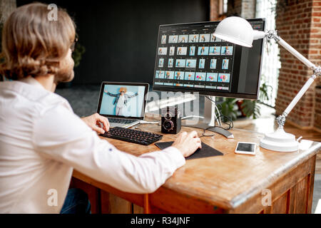 Macho joven fotógrafo que trabaja con retratos de mujer sentada en el lugar de trabajo con dos ordenadores en el studio