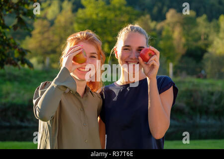 Dos niñas, mujeres jóvenes, riendo, comiendo manzanas en el jardín, la Alta Baviera, Baviera, Alemania