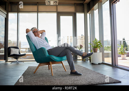 Hombre maduro sonriente relajado en un sillón en la ventana en casa Foto de stock