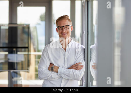Retrato del hombre de negocios sonriendo en la oficina, apoyada contra la ventana