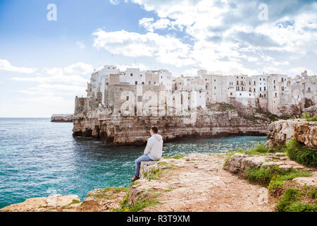 Italia, Apulia, Polognano a Mare, vista posterior del hombre descansando en las rocas mirando al horizonte