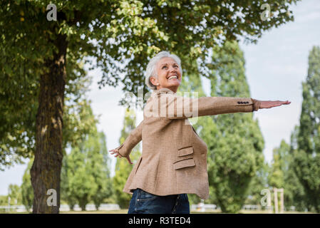 Feliz mujer mayor con los brazos estirados en un parque