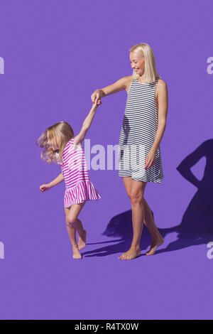 Madre e hija en rayas vestidos bailando en el fondo púrpura Foto de stock