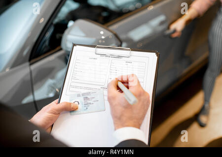 Gerente de servicio del vehículo llenado documentos celebración carpeta con  licencia de conducir en el showroom con el coche en el fondo Fotografía de  stock - Alamy