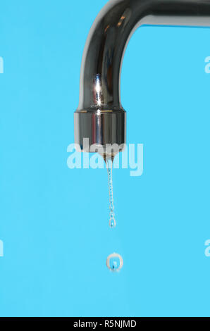 El agua que fluye desde la llave de paso closeup sobre fondo azul. Foto de stock