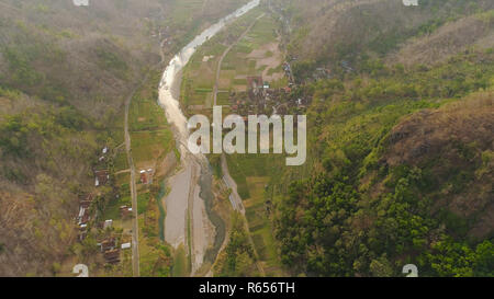 Vista aérea del río Barranca Oyo entre terrazas de arroz de las tierras de río en el cañón de montaña Kebun Mangunan Buah, Gorge, entre colinas cubiertas de vegetación, árboles al atardecer. paisaje tropical.