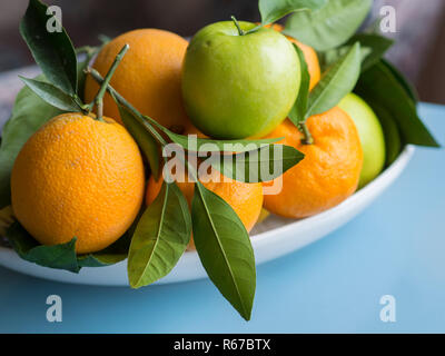Mandarina, naranja y manzana verde en la placa blanca. Frutas orgánicas de pie sobre un piso de madera con hojas
