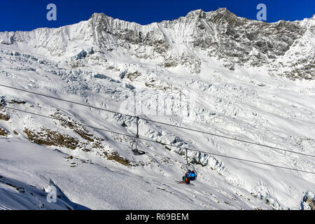 Los esquiadores en un telesilla contra el Canon Glaciar y el macizo del Mischabel, Saas-Fee, Suiza Foto de stock