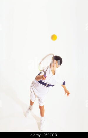 Retrato, Ganzfigur, Junge mit kurzen braunen Haaren, 12 Jahre, weisser Tenniskleidung beim Schlagen des balles mit dem Schlaeger Foto de stock
