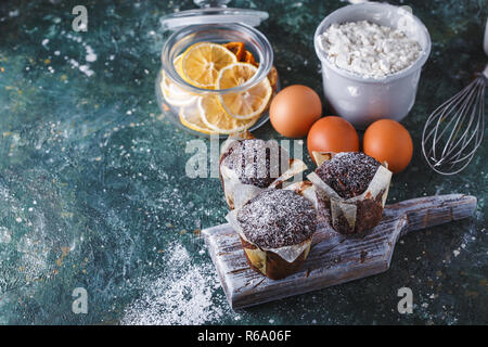 Zanahoria muffin de chocolate espolvoreado con azúcar impalpable, una taza de té, ingredientes para hornear. Harina, huevo, limón citrus sobre una tabla, copia espacio oscuro