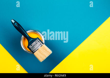 Cepillo en abrir la lata de pintura de color amarillo sobre fondo amarillo y azul. Piso estilo laical. Concepto de renovación.