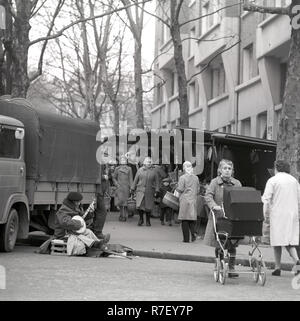 Las personas van de compras en un mercado semanal mientras un deshabilitado el banjo se sienta en el borde de la carretera en el barrio de Montmartre en París, Francia, en noviembre de 1970. Foto: Wilfried Glienke | uso en todo el mundo Foto de stock