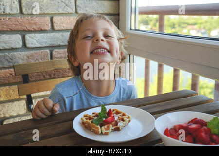 5 Feliz año viejo muchacho caucásico para comer el desayuno vienés de Gofres con helado y fresas. Foto de stock
