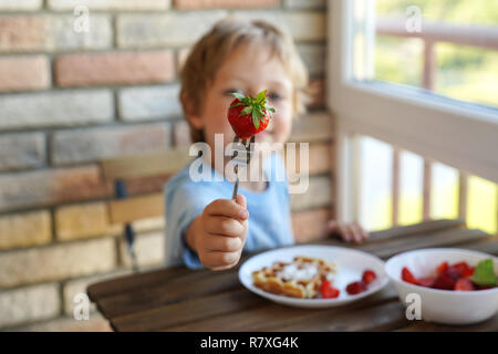 5 Feliz año viejo muchacho caucásico para comer el desayuno vienés de Gofres con helado y fresas. Foto de stock