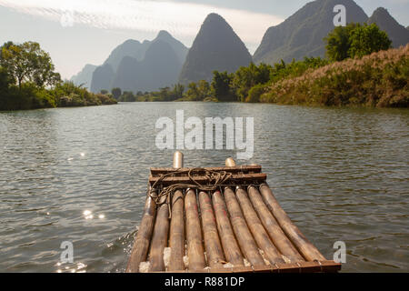 Delante de la balsa de bambú en primer plano sobre el río Yulong, Yangshuo, China. Acantilados de piedra caliza en silueta a lo largo del borde del río. Foto de stock