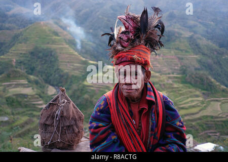 Un anciano Ifugao hombre llevando sombreros adornados con plumas y monkey cráneo en las terrazas de arroz de Banaue.... en el norte de Luzón, Filipinas. En el pasado los Ifugao, también conocido como el Ifugaw, Yfugao Ipugao, eran de temer head-hunters, así como otras tribus en las regiones montañosas del norte de Luzón. Foto de stock