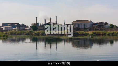 Ver a través de un gran río Nilo en Egipto, a través de los paisajes rurales con caña de azúcar indutrial causando contaminación en fábrica Foto de stock
