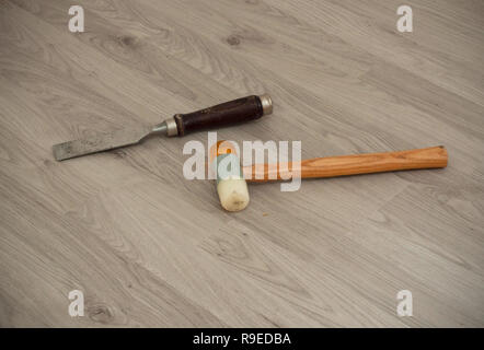 Un cincel metálico con mango de madera y un martillo en el laminado especial de fondo. Herramientas y material utilizado para pisos Foto de stock
