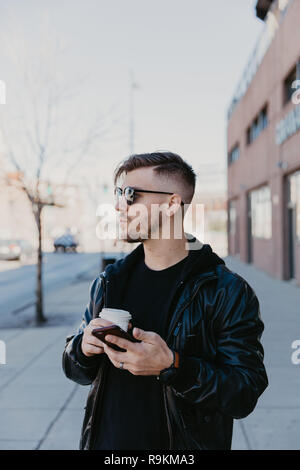Feliz joven macho milenario Hombre empresario de negocios en el centro de la metrópoli urbana en su Celular, mensajes de texto y llamadas telefónicas de negocios, tomando café