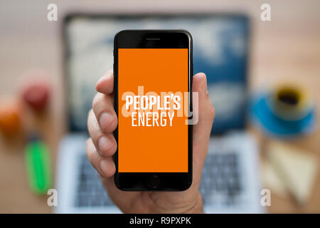 Un hombre mira el iPhone que muestra el logotipo de energía del pueblo (uso Editorial solamente). Foto de stock