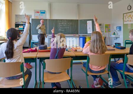 Los estudiantes de escuela elemental con manos levantadas en el aula, Baja Sajonia, Alemania