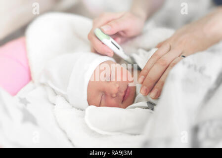 Bebé en la cuna mide la temperatura corporal. Mamá mide la temperatura corporal del bebé con un termómetro. Foto de stock