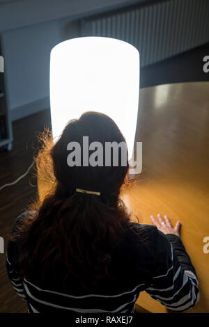 La terapia de luz con lámpara de luz diurna, una mujer sentada delante de una lámpara que imita la luz diurna, terapia contra la depresión en el invierno, porque hay demasiado poca