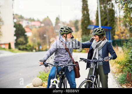 Personas mayores activas con saludo electrobikes afuera en una carretera en la ciudad.