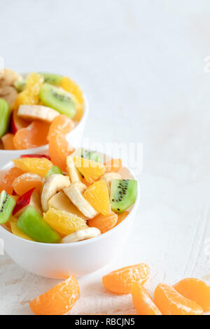 Dos cuencos blancos con ensalada de frutas y mandarín en rodajas sobre fondo blanco. Foto de stock