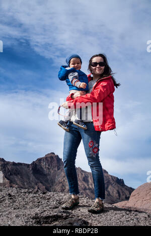 Una bonita foto de una bella mujer y su hijo de pie sobre una montaña en el fondo de un cielo nublado