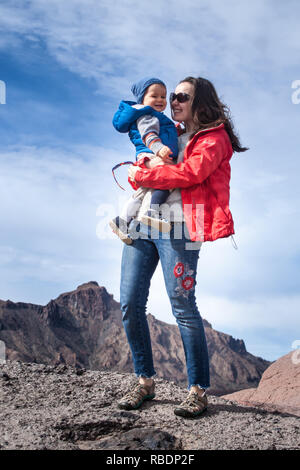 Una bonita foto de una bella mujer y su hijo de pie sobre una montaña en el fondo de un cielo nublado