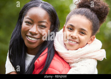 Joven negra aprovechar su pre-adolescente hija en el parque, ambas sonriendo a cámara, cerrar
