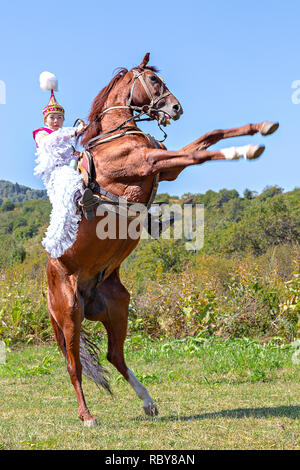 Mujer kazaka en trajes nacionales, levantándose su caballo, en Almaty, Kazajstán. Foto de stock