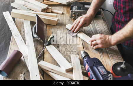 Carpintero trabajando en un taller de carpintería. Hombre lijado tablón manualmente Foto de stock