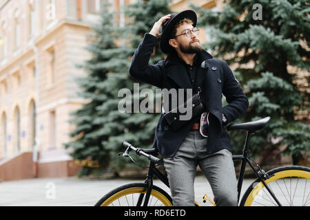 Retrato del hombre hipster urbano en gafas de sol y sombrero posando con bicicleta
