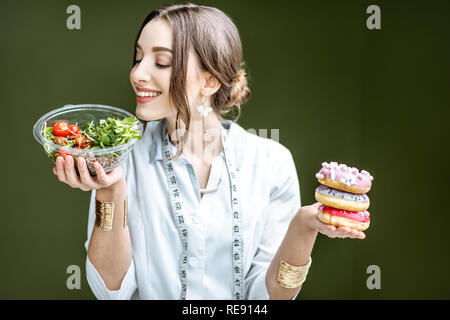 Mujer joven nutricionista mirando en la ensalada elegir entre comida sana y dulce postre en el fondo verde