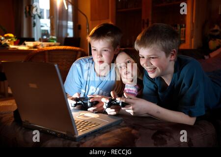 Hermanos, 7, 11, 13 años de edad, con ordenador portátil en el salón, jugando a un videojuego de carreras de coches