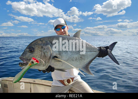 La pesca en alta mar, la pesca del juego grande. Feliz pescador sosteniendo un trevally jack Foto de stock