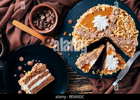 Torta de maní, coronado con crema de mantequilla de cacahuete cacao y claras de huevo roses sirve sobre una placa negra sobre una tabla de madera rústica con café en taza de loza Foto de stock