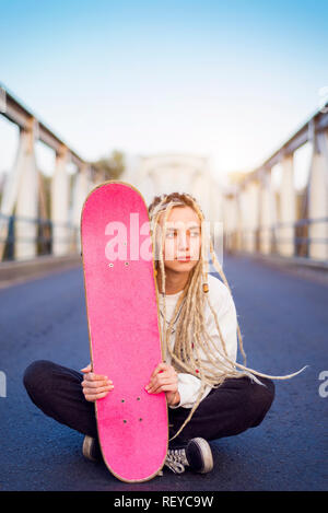 Mujer joven sentado en el puente con el retrato de skate Foto de stock