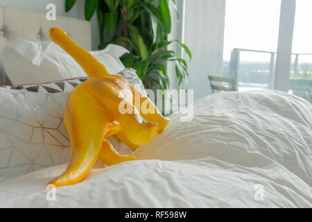 Dinosaurio de juguete amarillo en cama de padres de crianza, representando el estilo de vida y un verdadero hogar. Foto de stock