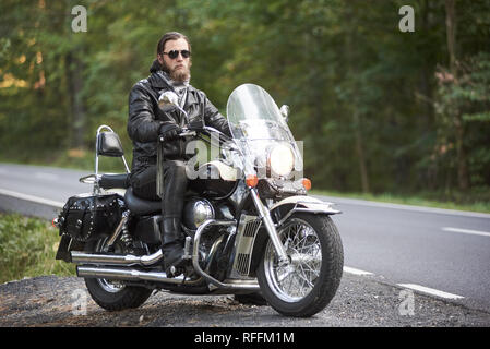 Apuesto motociclista en ropa de cuero negro y gafas sol oscuras viajando en moto por carretera del país sobre los antecedentes de una recta vacía Fotografía de stock - Alamy