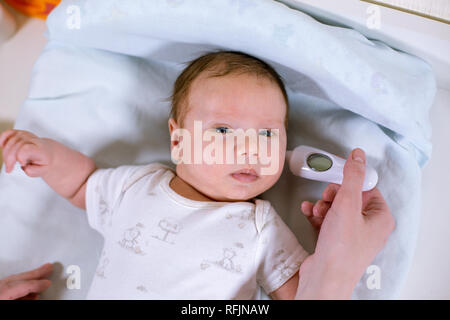 Medir la temperatura del bebé con termómetro sin contacto. Mamá mide la temperatura corporal del bebé con un termómetro en el oído. Foto de stock
