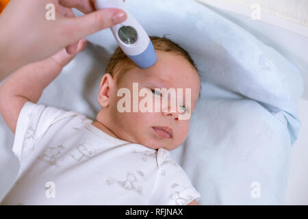 Medir la temperatura del bebé con termómetro sin contacto. Mamá mide la temperatura corporal del bebé con un termómetro Foto de stock