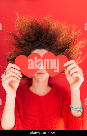 Vista superior de Chica sujetando las tarjetas en forma de corazón en la parte delantera de la cara aislado en rojo, San San Valentín concepto